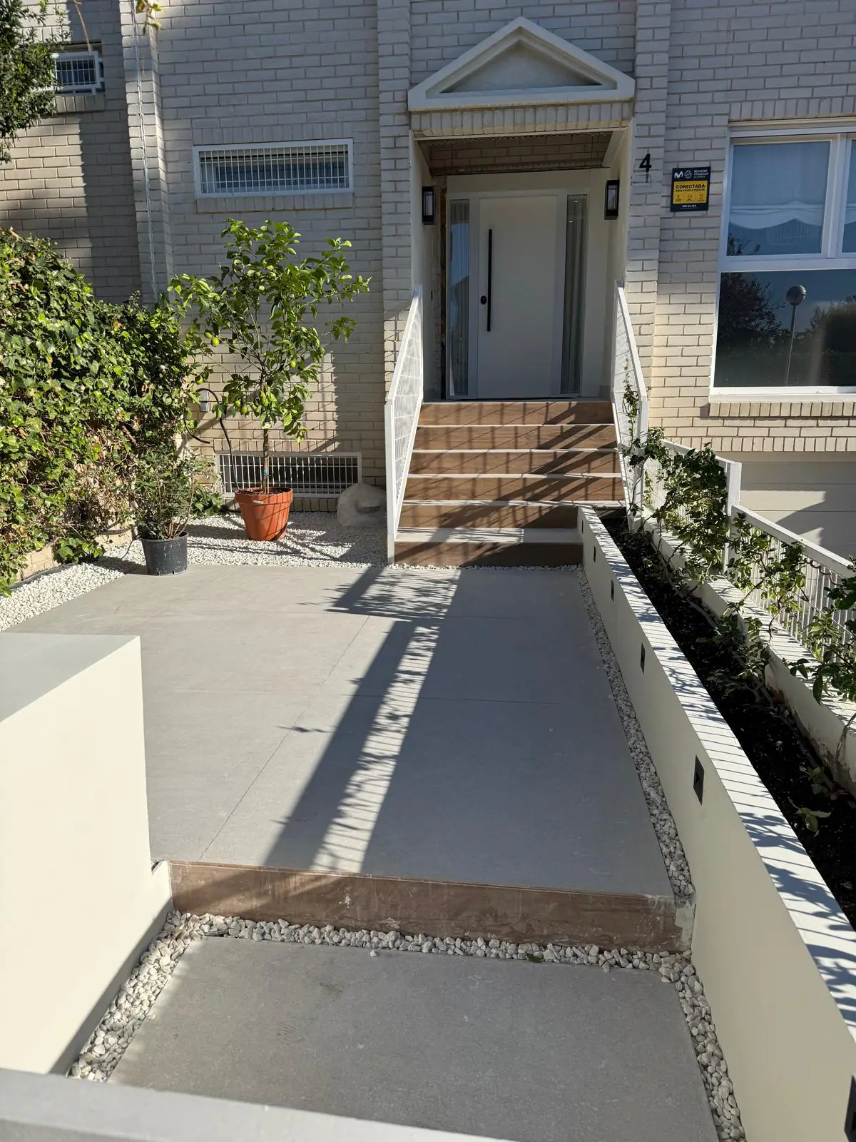 Entrada reformada con suelo porcelánico gris, escalones en acabado madera, jardineras y grava blanca